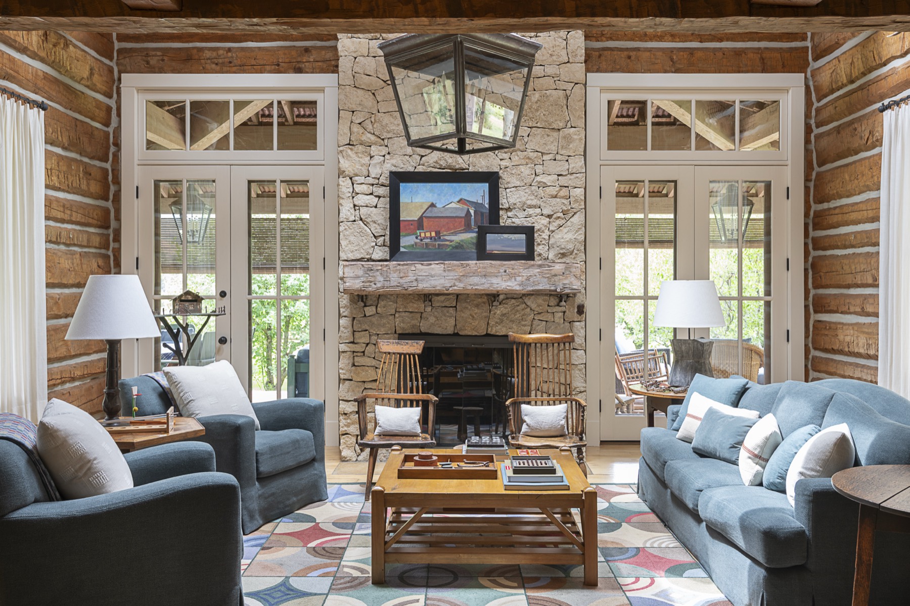 Log-walled living room with a stone fireplace, blue sofas, and small barn paintings on the mantel