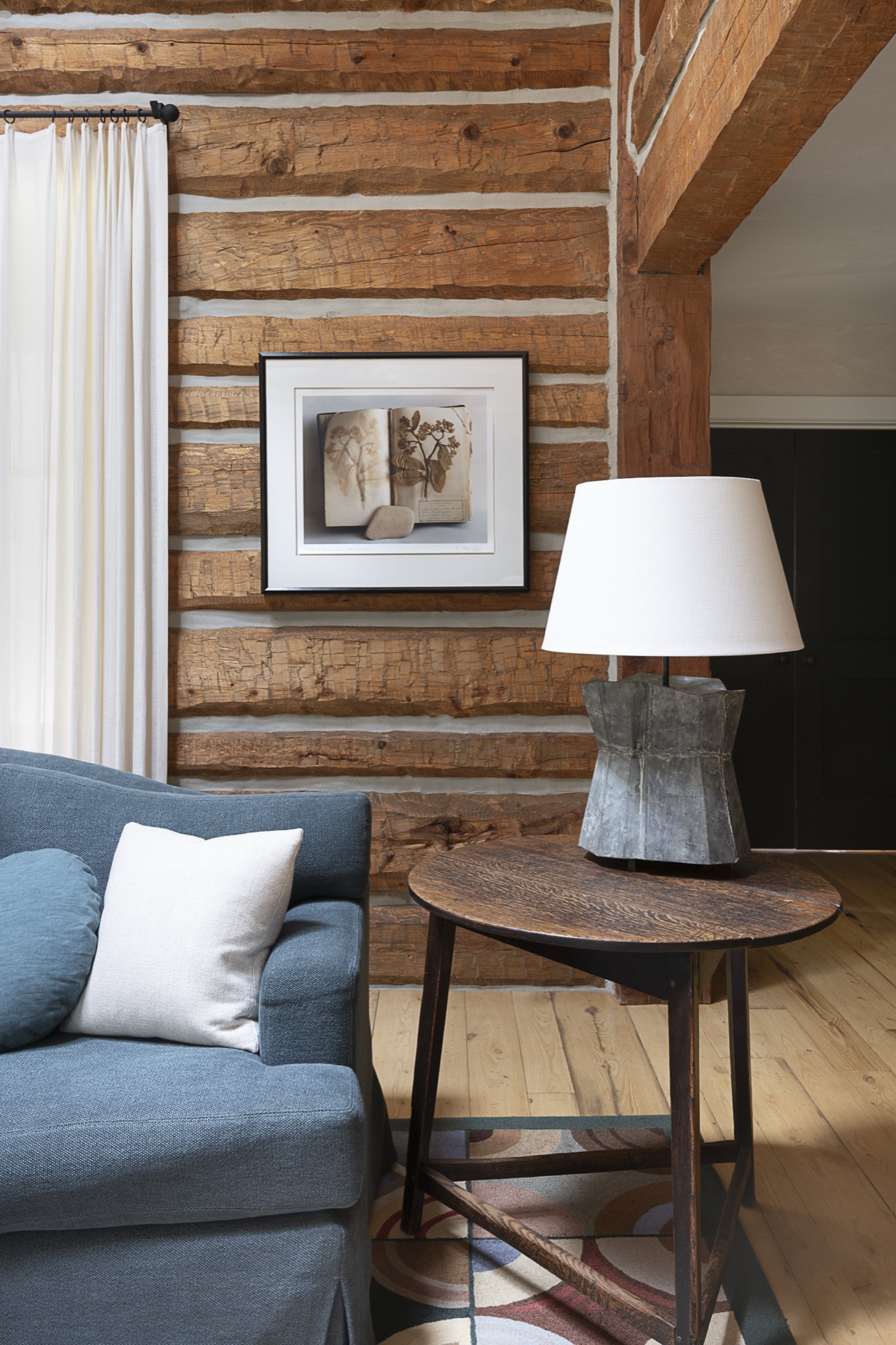 Framed pressed-botanical photograph on a log wall beside a blue sofa