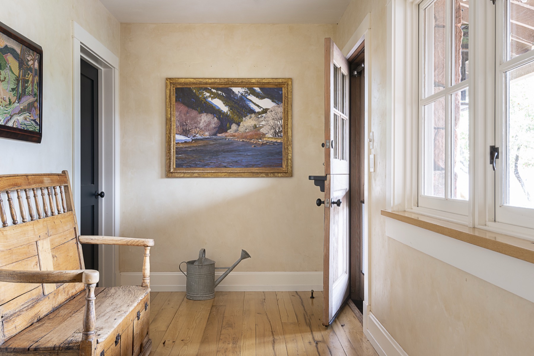 Gold-framed river and mountain landscape painting in a sunlit entry hall