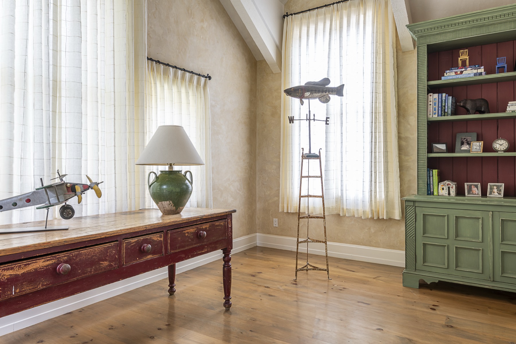 Study with a fish weathervane, a green bookcase, and a model airplane on a red console table