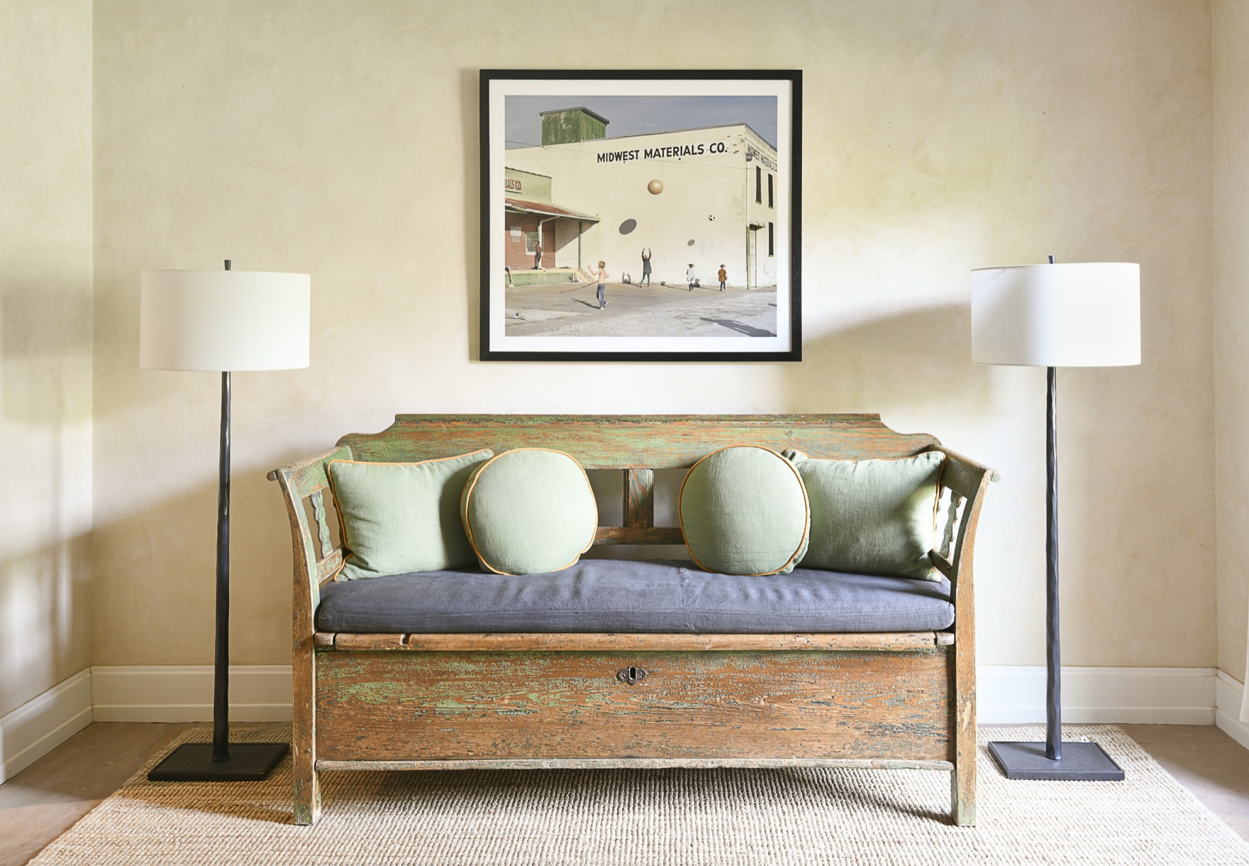 Framed Midwest Materials photograph above a distressed green bench, flanked by floor lamps