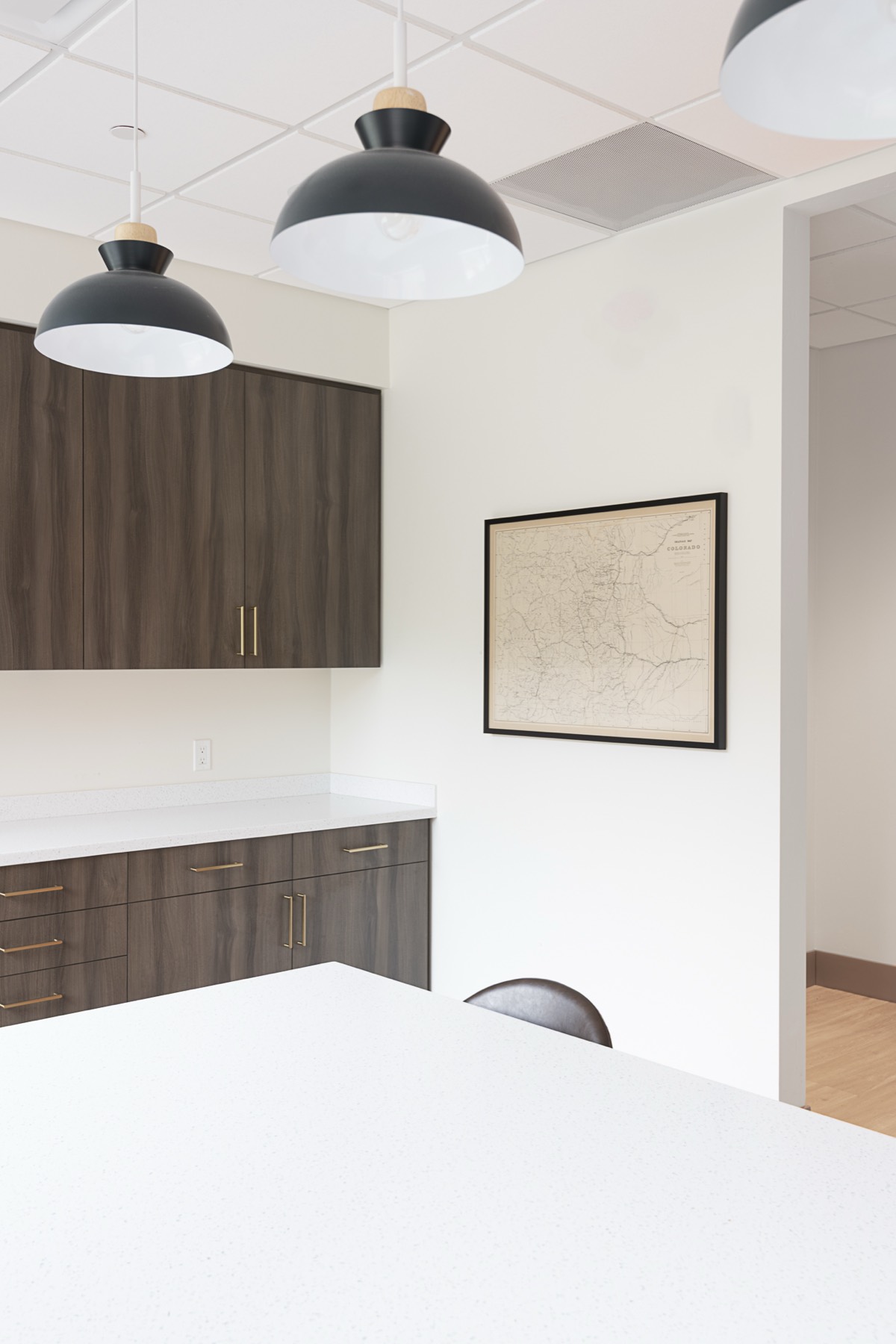 Framed vintage map of Colorado on the office kitchen wall beneath black pendant lights