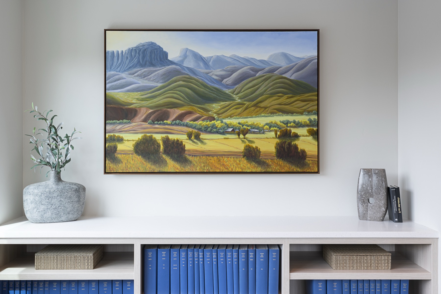Original oil painting of a Colorado valley and mountains, framed above a console with a vase and books