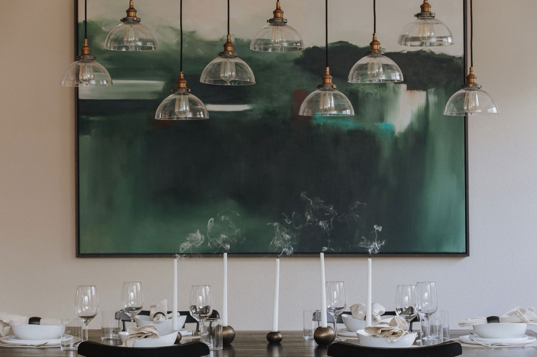 Large green abstract painting above a dining table set with candles and white dishware