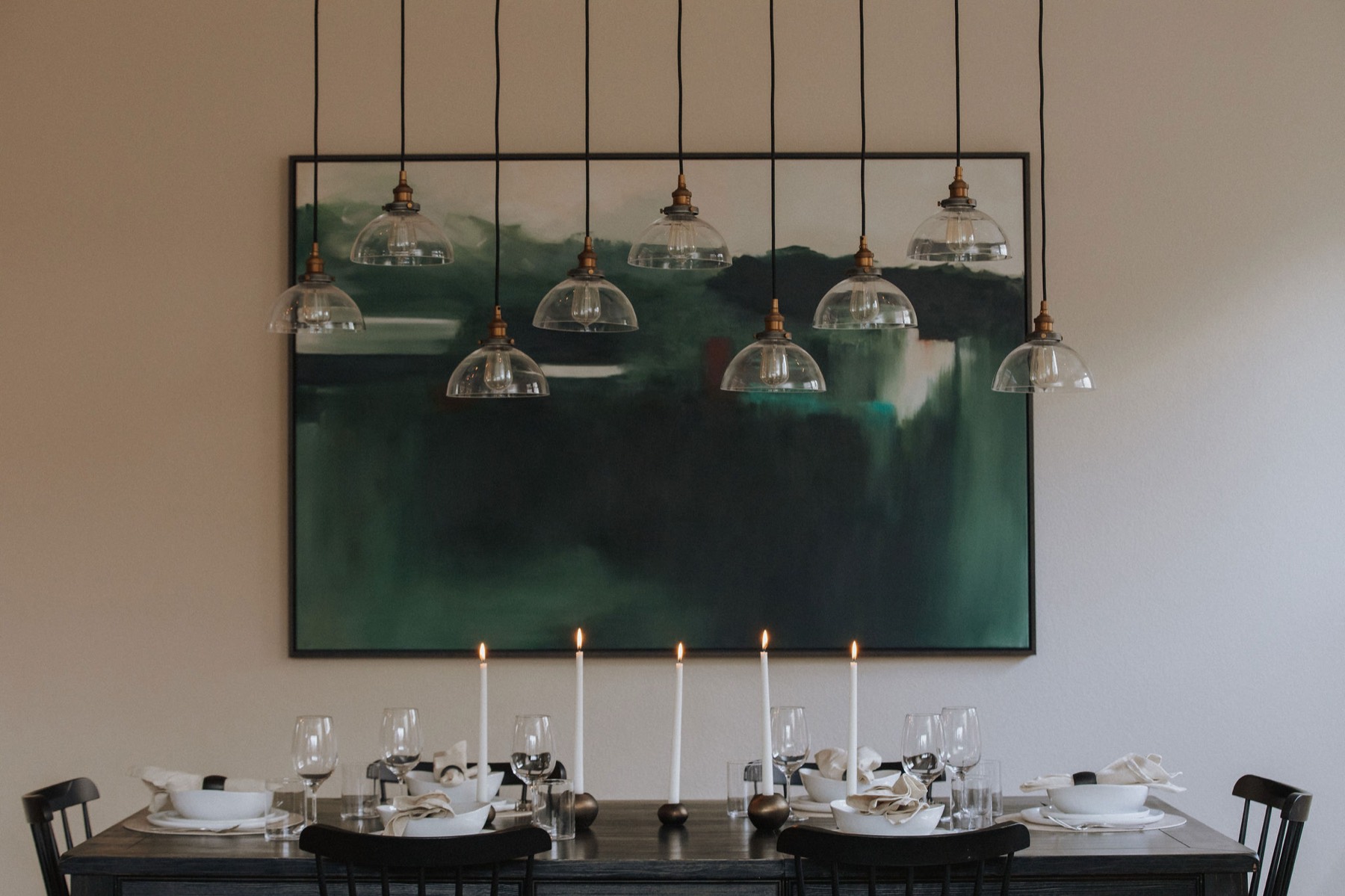The green abstract painting seen across the full dining table at dusk