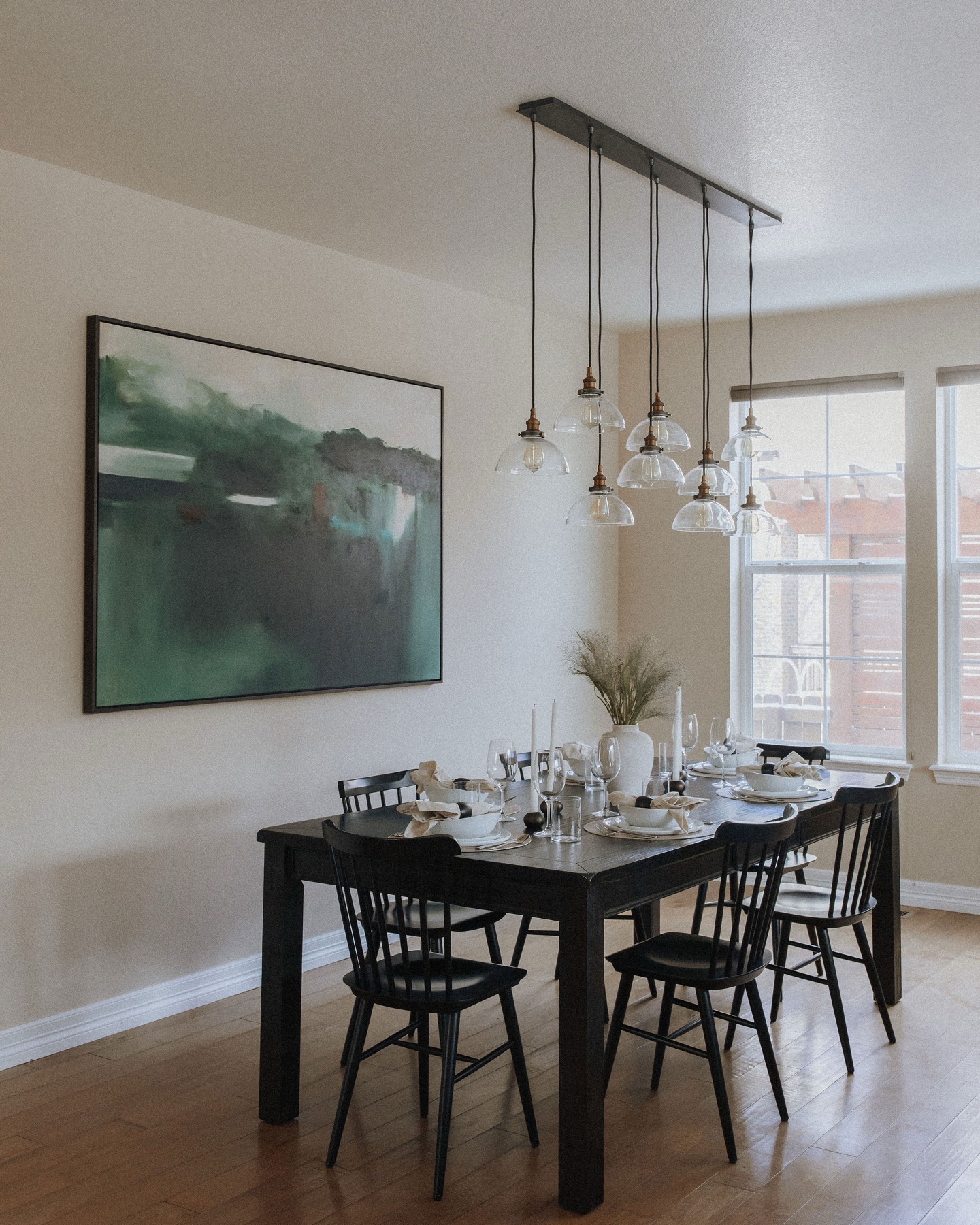 Wide view of the dining room with the green abstract painting beside sunlit windows