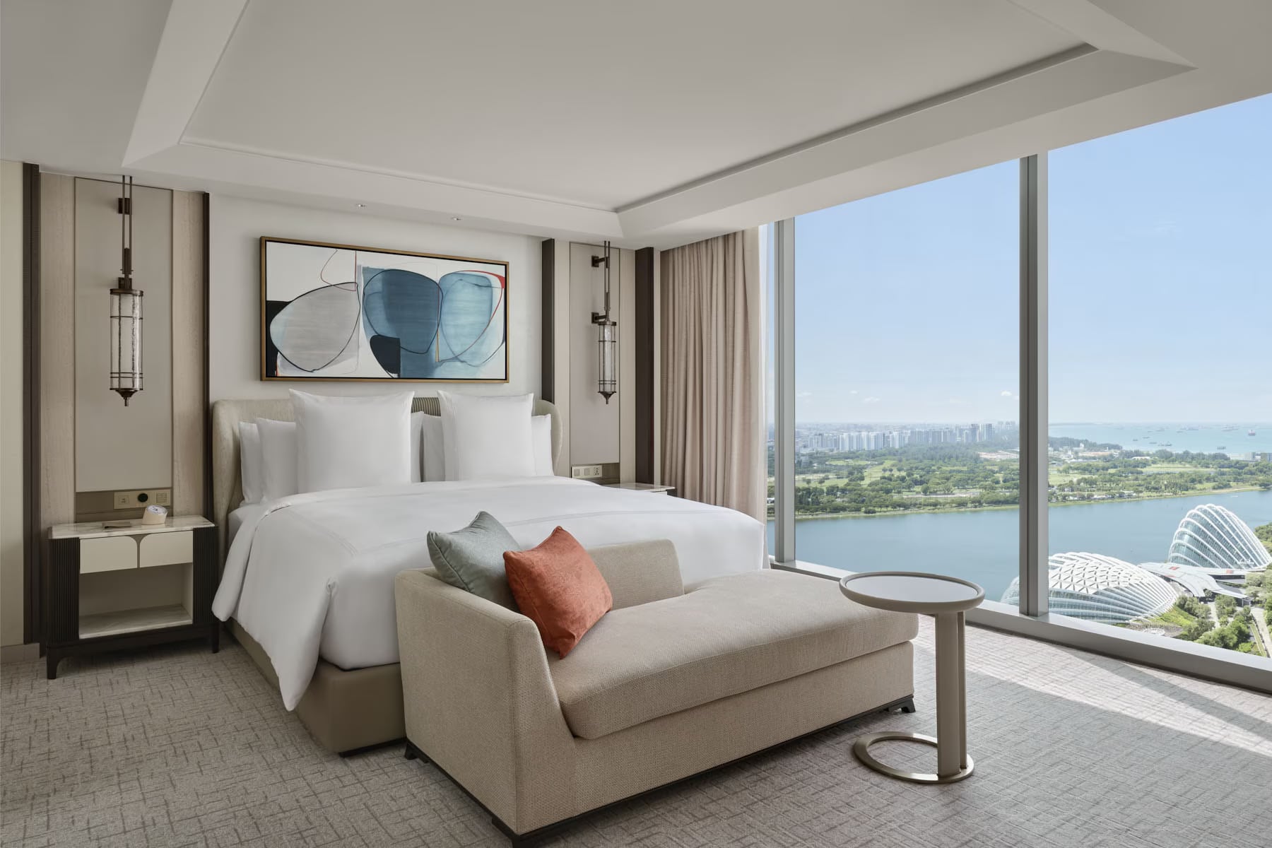 A Paiza Premier suite bedroom: a soft blue watercolor abstract above the bed, a coral pillow, and Marina Bay through the window