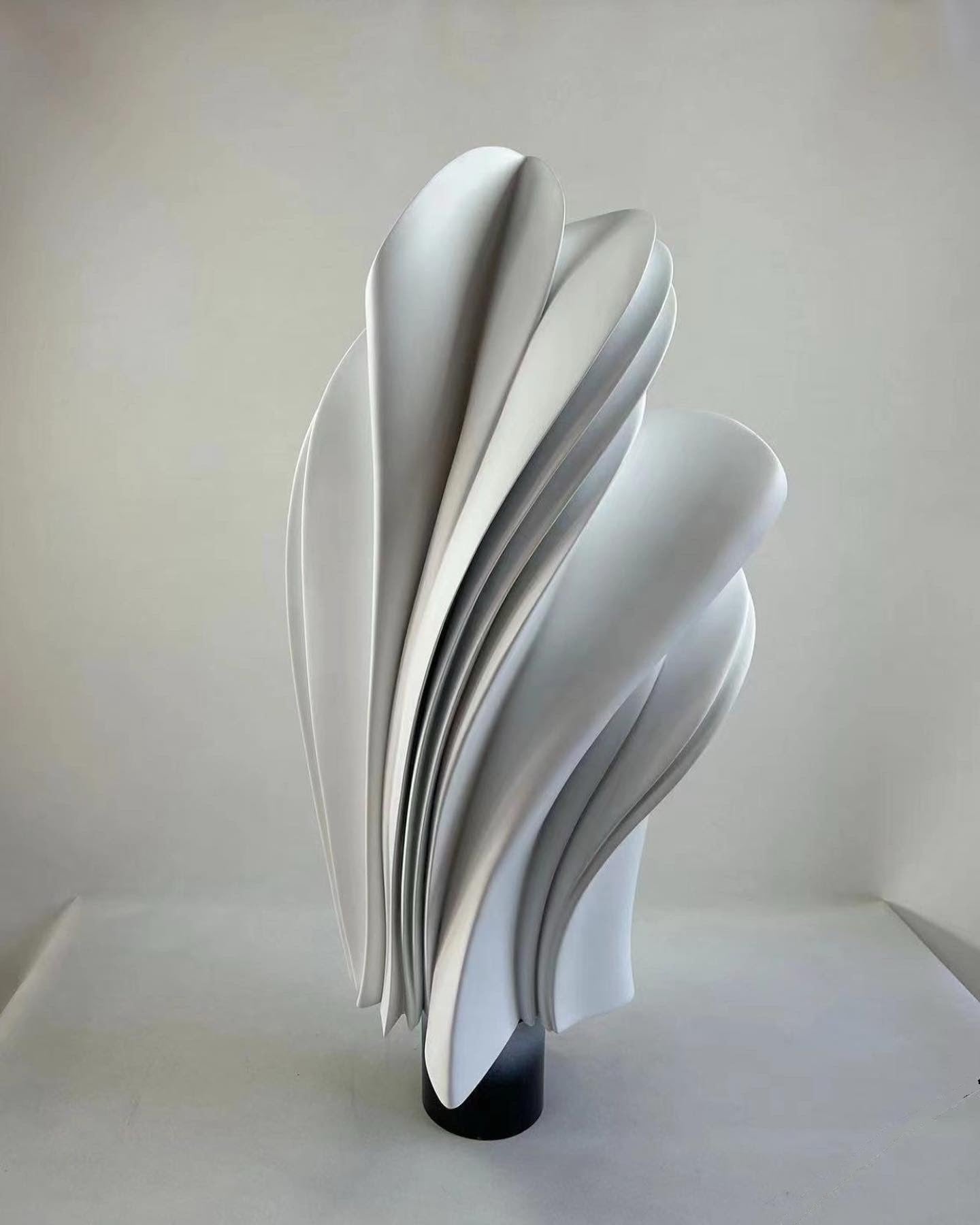 A tall white sculpture of pleated, wave-like folds rising from a dark base, commissioned for the Paiza Collection