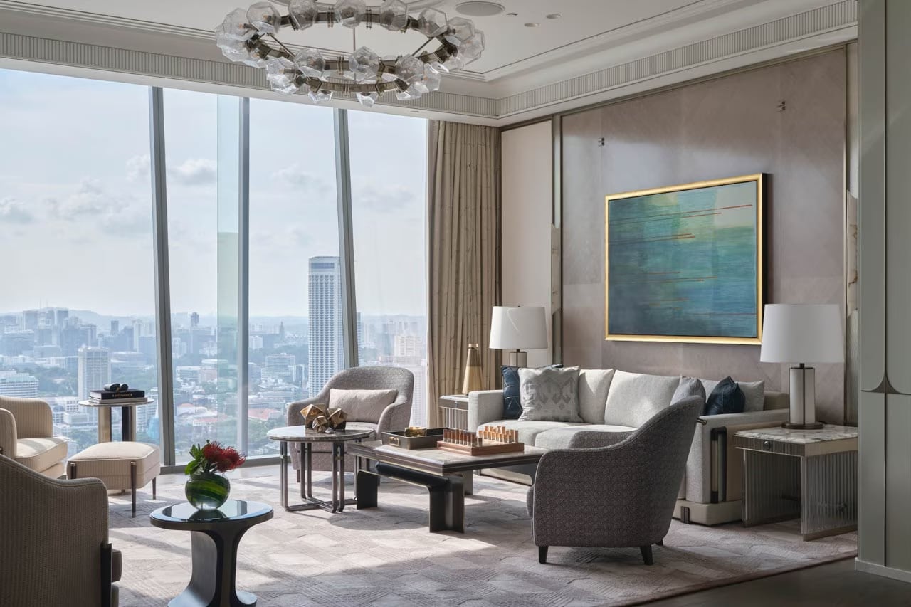 A Paiza suite sitting room: a gold-framed abstract of sea and sky above the sofa, a crystal chandelier, and Singapore's skyline through the window