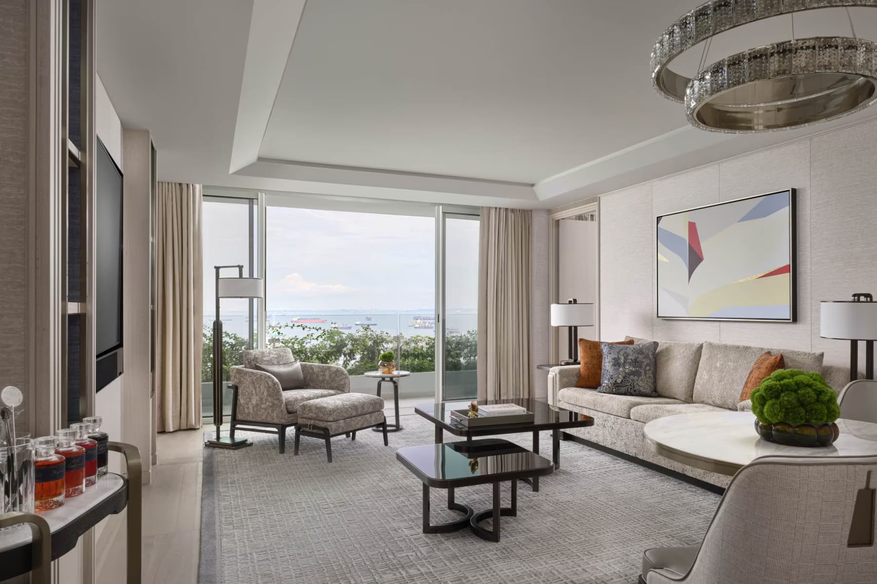 A Paiza Premier suite living room: a light abstract painting above the sofa, a round crystal pendant, and the sea view beyond