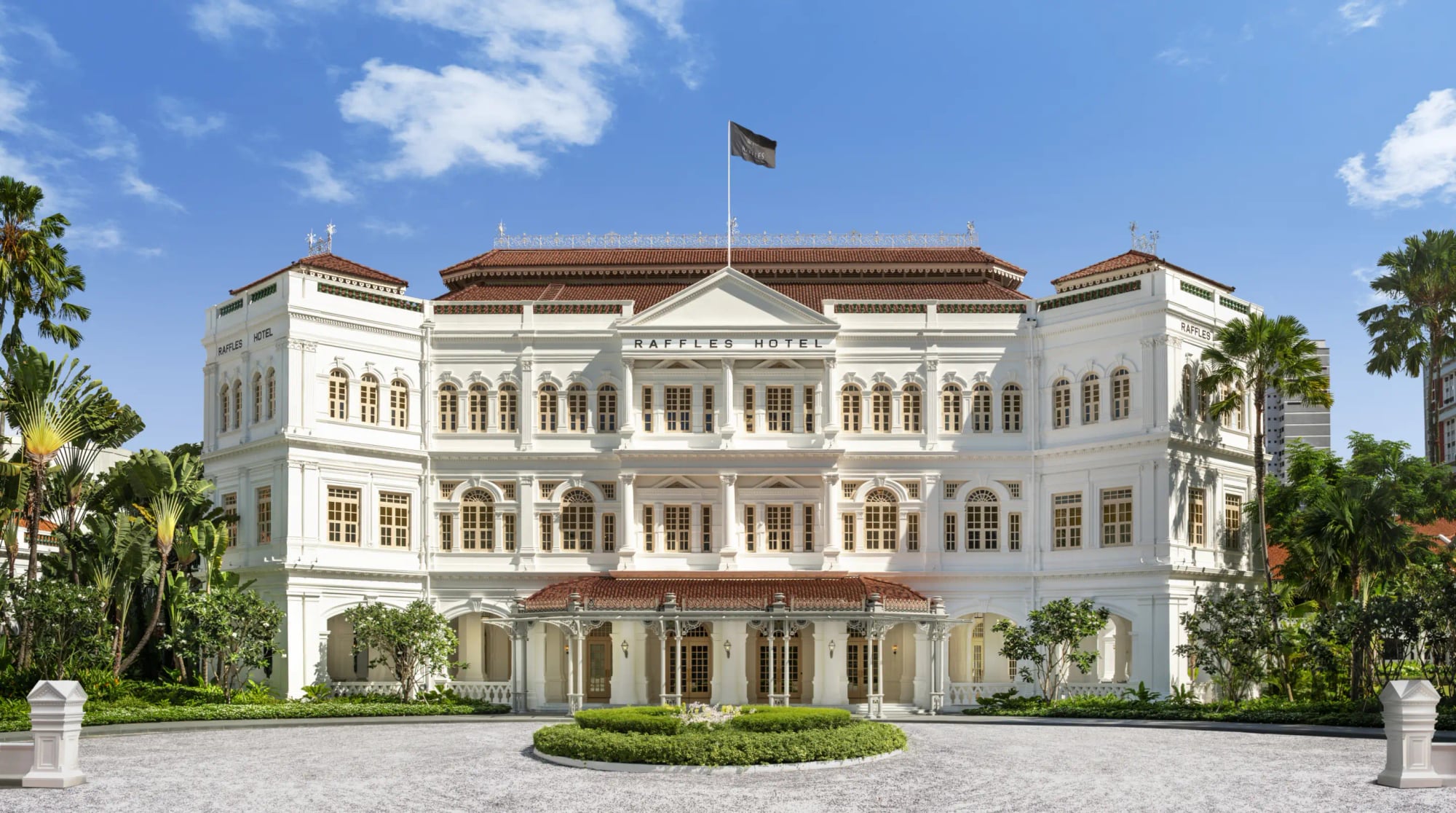 The white Neo-Renaissance facade of Raffles Singapore, with its arched verandas, palm trees, and the front drive