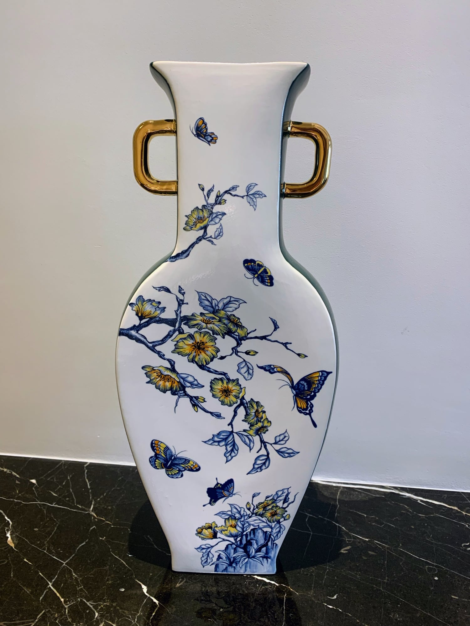 A blue-and-white porcelain vase painted with butterflies and blossoms, with gold handles, on a dark marble surface