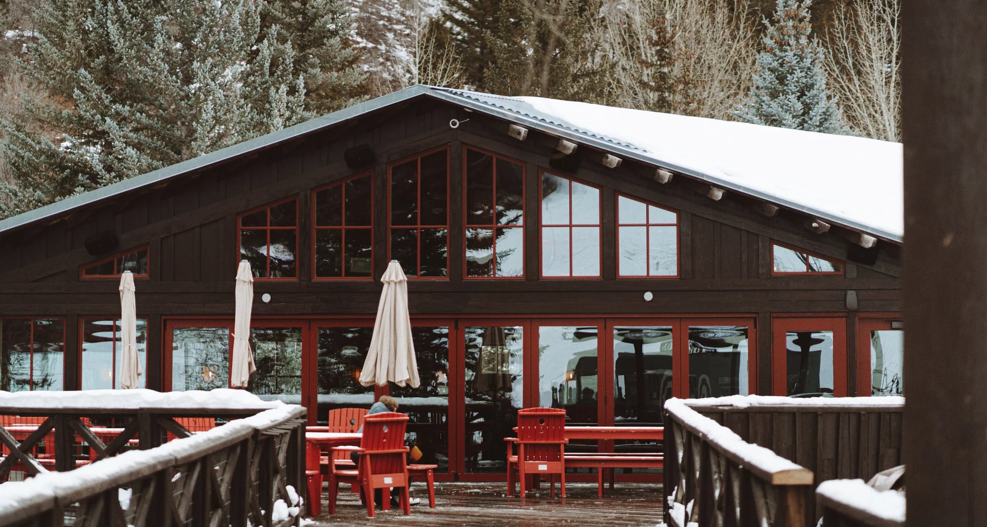 The Lookout restaurant at Sundance Mountain Resort: dark timber facade with red-framed windows, folded umbrellas, and red Adirondack chairs on a snow-covered deck