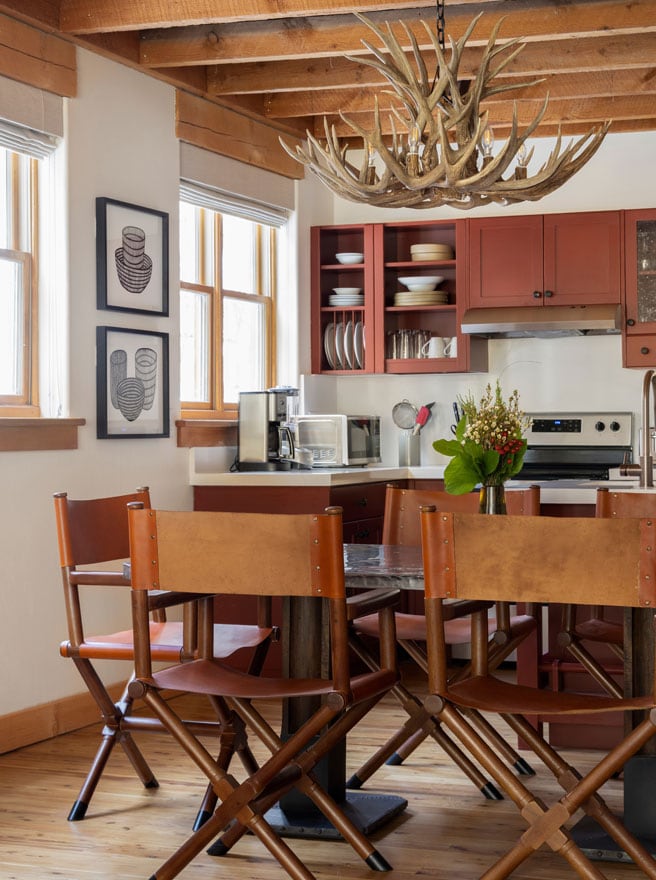 Model room kitchen with a pair of framed black-and-white line drawings of vessels beside the window, red cabinets, and an antler chandelier