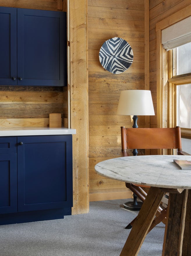 Woven black-and-white basket hung as wall art on timber planking beside a leather chair, lamp, and marble table in the model room