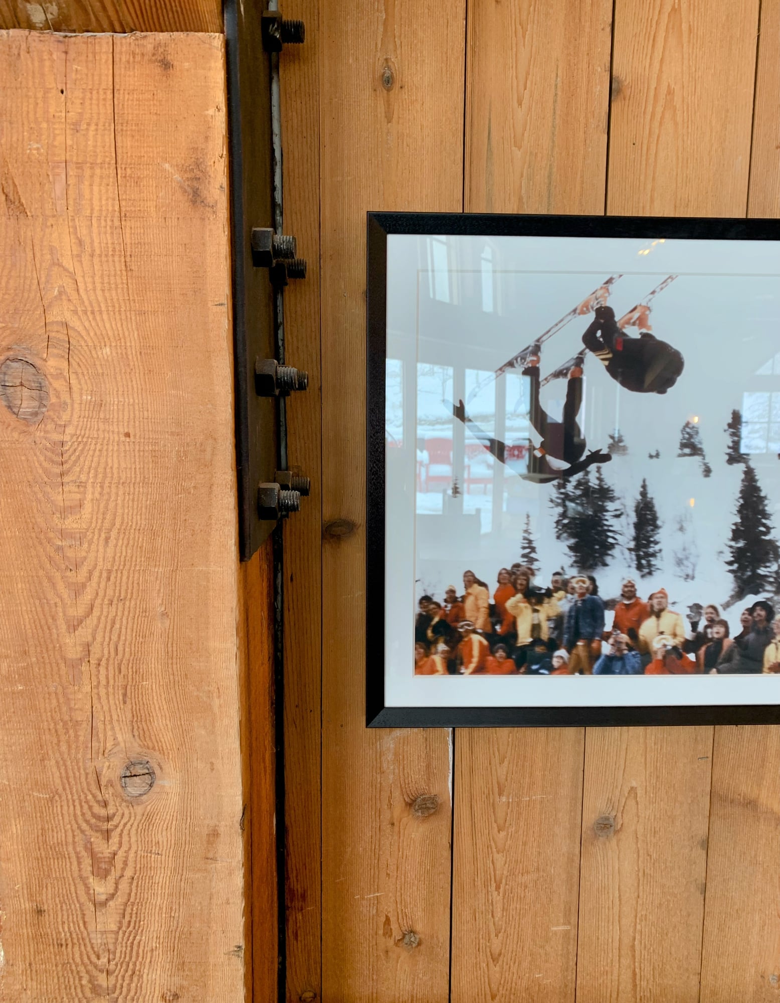 Detail of a framed vintage photograph of an aerial skier above a crowd in orange, hung beside a bolted timber post at The Lookout