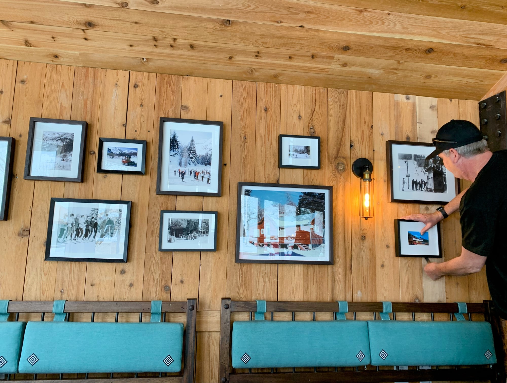 Installing the gallery wall at The Lookout: framed vintage ski photographs going up on cedar planking above teal banquettes